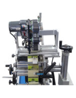 Κοντινή όψη του μηχανήματος με τα γρανάζια και τα καρούλια που περνάει η αυτοκόλλητη ετικέτα για την επικόλλησή της στην συσκευασία που περνάει από την ταινία ροής από κάτω.